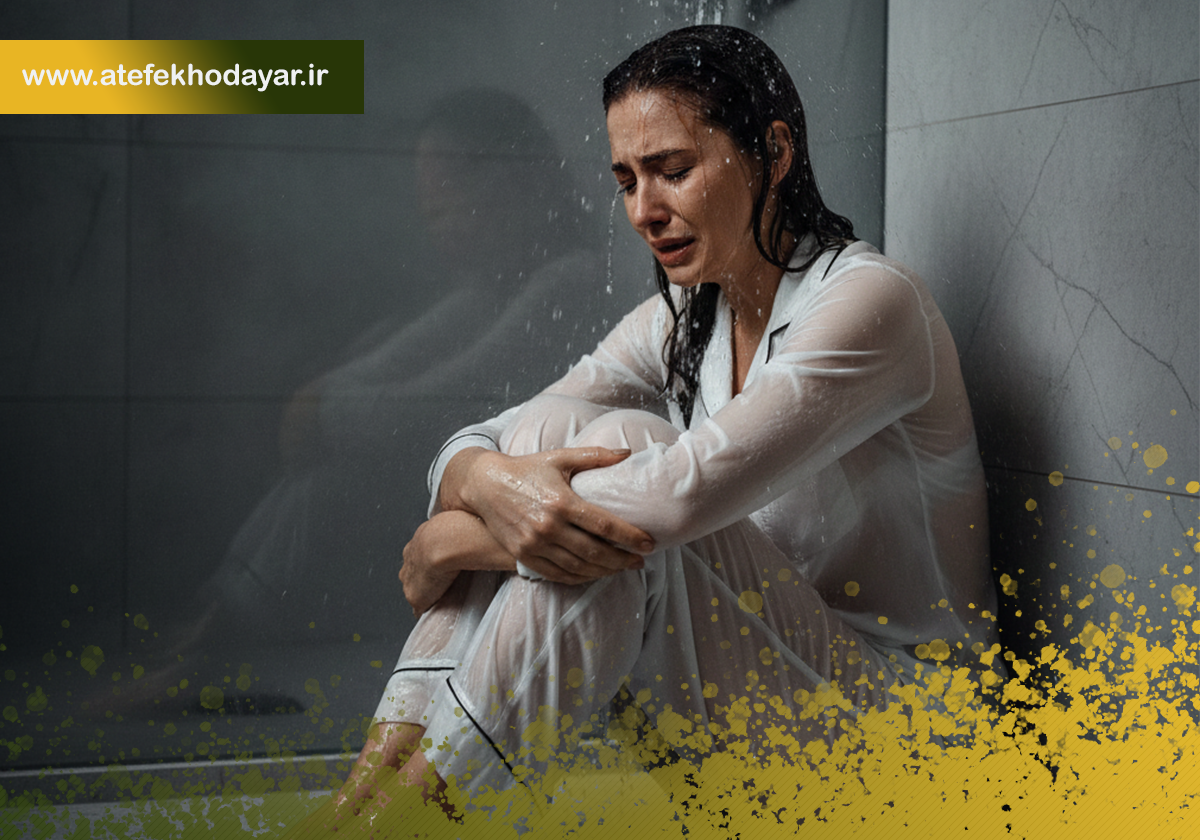 زنی با لباس خواب روی زمین حمام نشسته، آب دوش روی سرش میریزد و گریه میکند